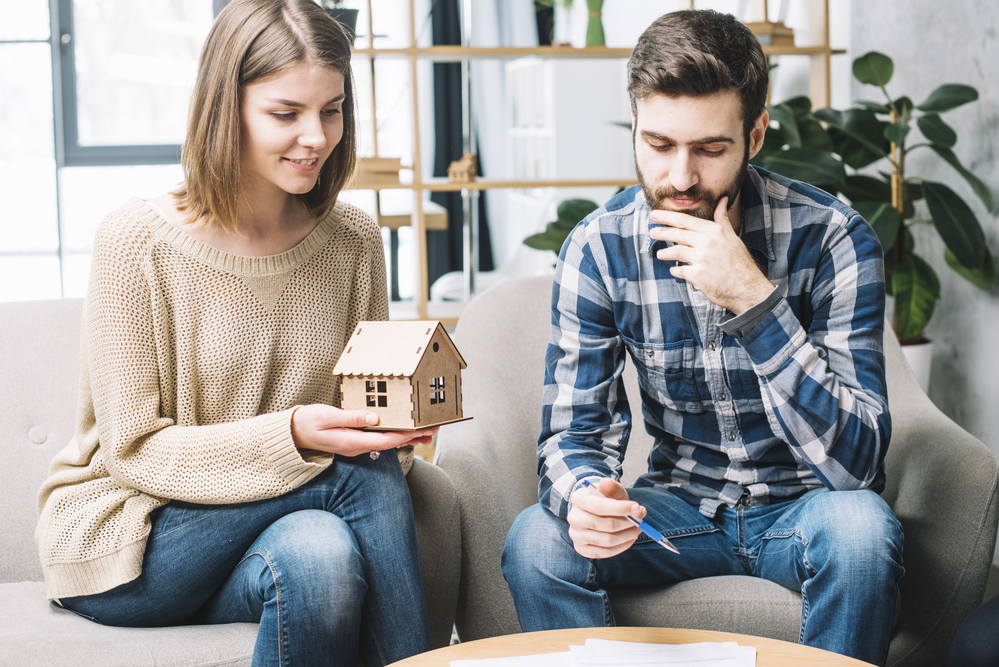 Jeune couple envisageant d’acheter une maison à La Réunion, tenant une maquette de maison.