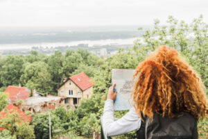 Femme consultant une carte face à une maison abandonnée à vendre en Gironde, au cœur d'un paysage verdoyant surplombant la Garonne.