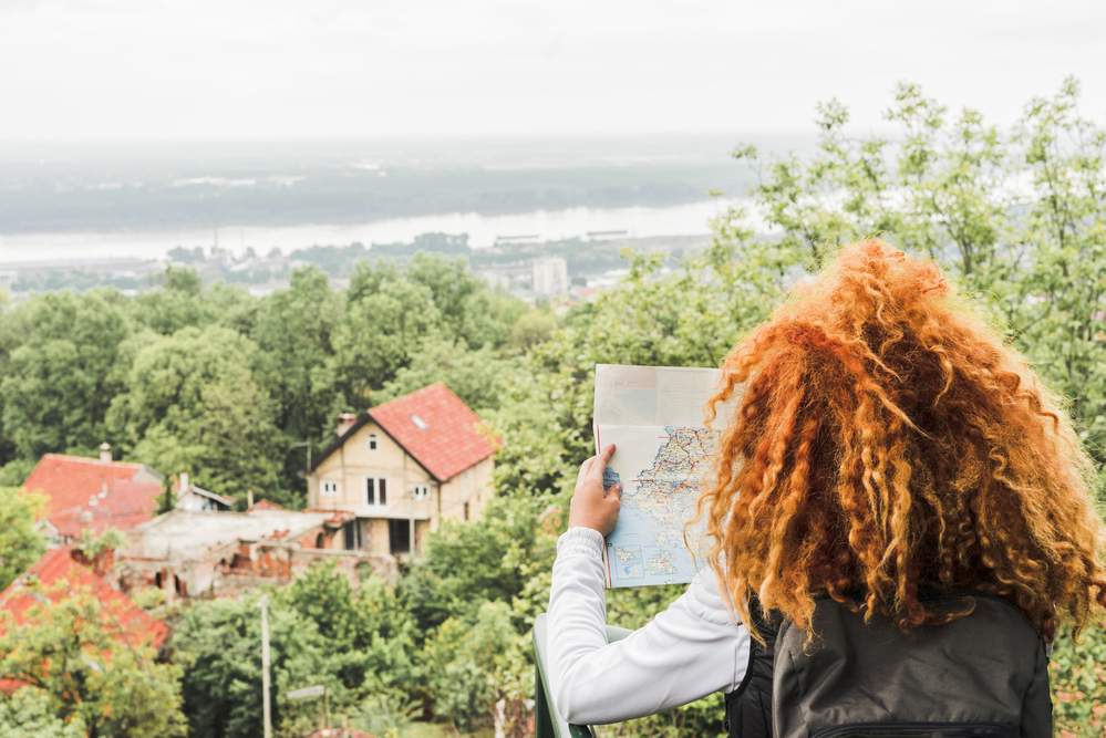 Femme consultant une carte face à une maison abandonnée à vendre en Gironde, au cœur d'un paysage verdoyant surplombant la Garonne.